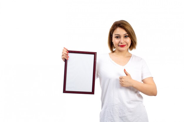 Una vista frontal jovencita en camiseta blanca con marco de fotos burdeos sonriendo en el blanco