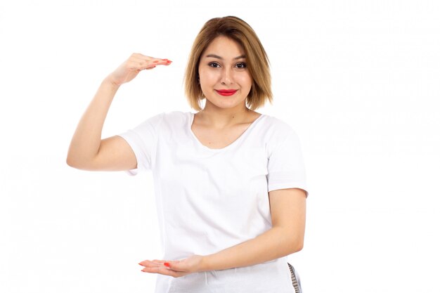 Una vista frontal jovencita en camiseta blanca posando mostrando tamaño sonriendo en el blanco