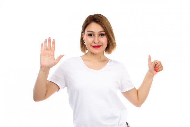 Una vista frontal jovencita en camiseta blanca posando sonriendo mostrando como signo en el blanco