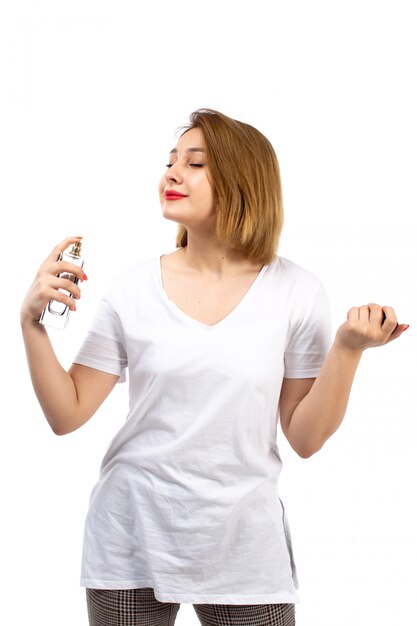 Una vista frontal jovencita en camiseta blanca con tubo de perfume negro usándolo en el blanco