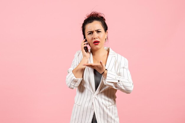 Vista frontal jovencita en chaqueta blanca hablando por teléfono sobre fondo rosa moda mujer emoción sentimiento dama color