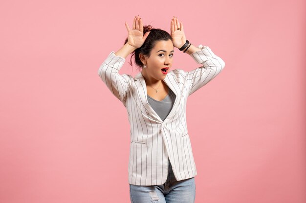 Vista frontal jovencita con chaqueta blanca posando sobre un fondo rosa claro moda mujer emoción color sentimiento dama