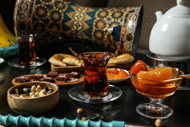 Vista frontal del juego de té té en un vaso armudu con mermelada, dulces nueces con pasas y una barra de chocolate sobre la mesa