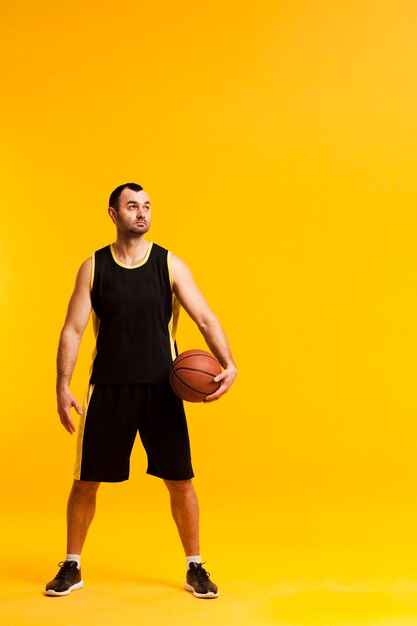 Vista frontal del jugador de baloncesto posando con balón cerca de la cadera y copia espacio