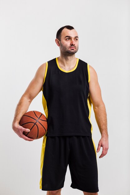 Vista frontal del jugador masculino estoico posando con baloncesto cerca de la cadera