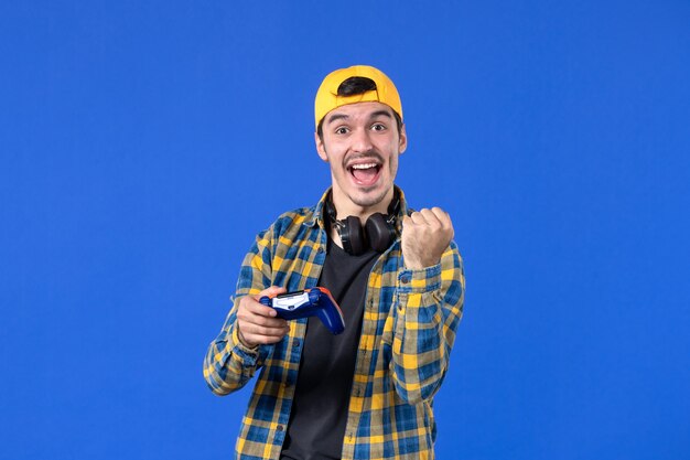 Vista frontal del jugador masculino con gamepad jugando videojuegos en la pared azul