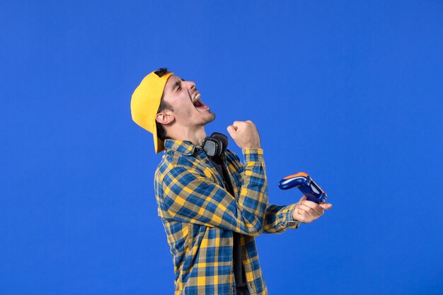 Vista frontal del jugador masculino con gamepad jugando videojuegos en la pared azul