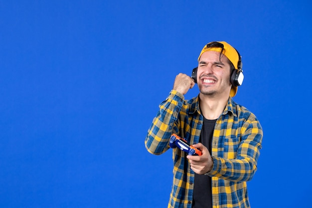Vista frontal del jugador masculino con gamepad jugando videojuegos en la pared azul