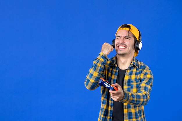 Vista frontal del jugador masculino con gamepad jugando videojuegos en la pared azul