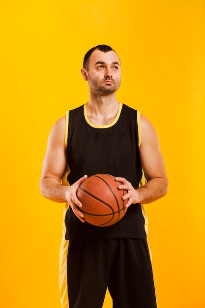 Foto gratuita vista frontal del jugador masculino posando mientras sostiene baloncesto