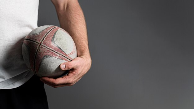 Vista frontal del jugador de rugby masculino sosteniendo la pelota junto a la cadera con espacio de copia