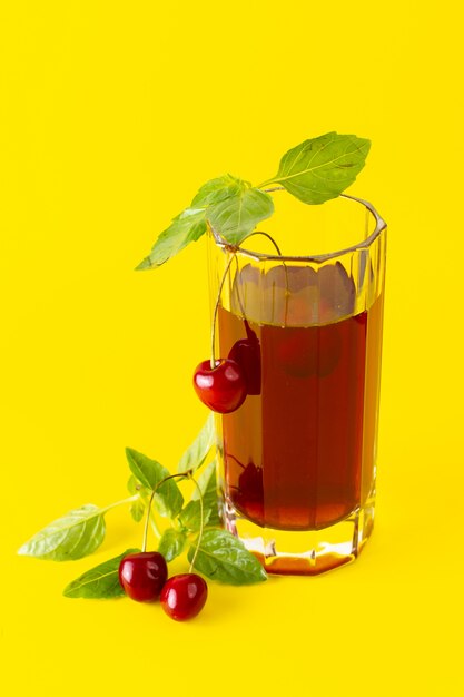 Vista frontal del jugo de cereza dentro de un vaso largo en la superficie amarilla