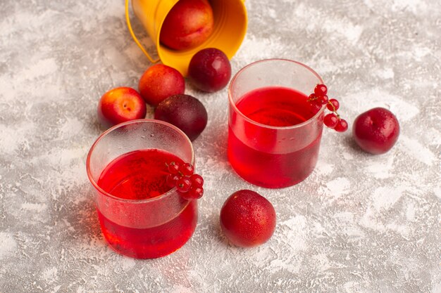 Vista frontal de jugo de ciruela de color rojo con ciruelas frescas en gris