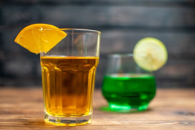 Vista frontal jugo de frutas frescas bebidas de naranja y manzana dentro de vasos en bebida de escritorio de madera marrón