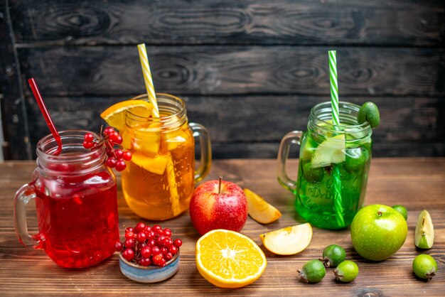 Vista frontal de jugo de frutas frescas, feijoa de naranja y bebidas de arándano dentro de latas en el escritorio marrón beber foto de color cóctel