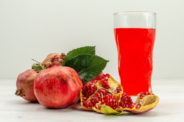 Vista frontal de jugo de granada fresca con granadas frescas sobre una superficie blanca clara