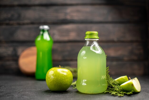 Vista frontal de jugo de manzana en botella manzana manzana cortada botella verde sobre superficie aislada de madera