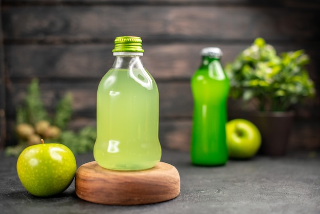 Vista frontal de jugo de manzana en botella sobre tablero de madera limonada manzana sobre superficie de madera oscura.