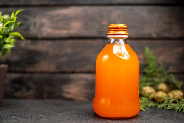 Vista frontal de jugo de naranja en botella de naranjas frescas sobre superficie aislada marrón