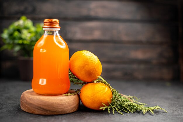 Vista frontal de jugo de naranja fresco en botella sobre tablero de madera