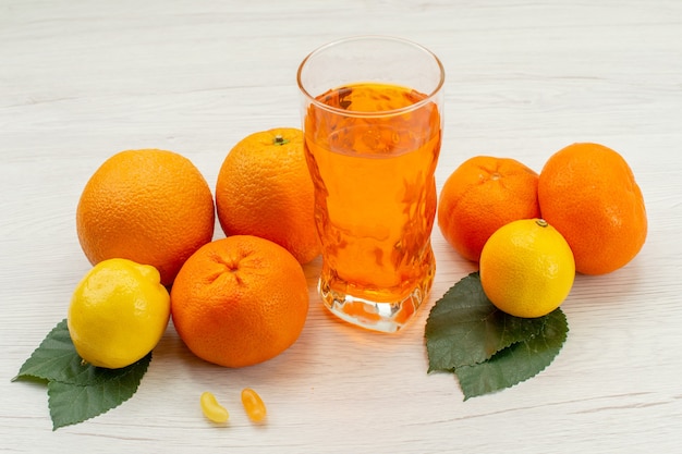 Vista frontal de jugo de naranja fresco con naranjas y cítricos en el escritorio blanco