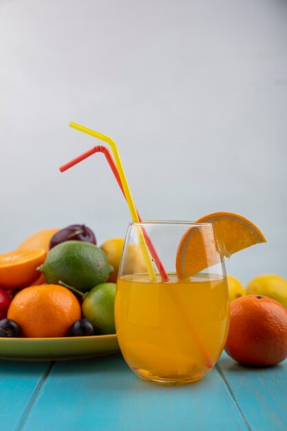 Vista frontal de jugo de naranja en un vaso con ciruela cereza naranjas ciruelas limones con lima en una placa amarilla