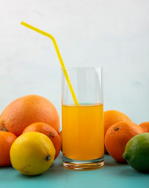 Vista frontal de jugo de naranja en un vaso y paja amarilla con naranjas pomelo y limón con lima