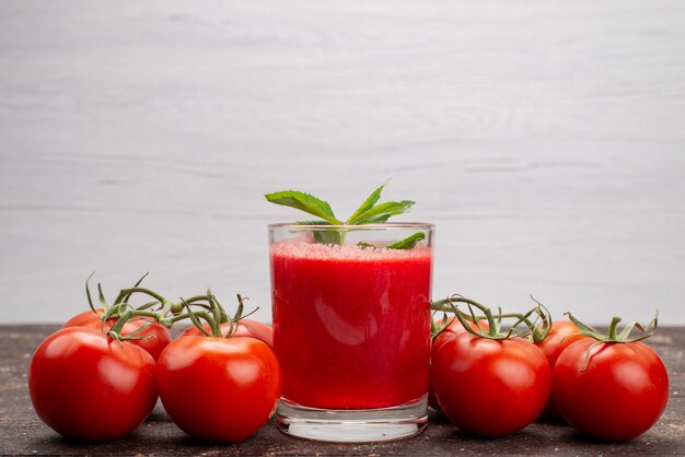 Vista frontal de jugo de tomate fresco con hojas junto con tomates enteros en cóctel de color gris, fruta vegetal