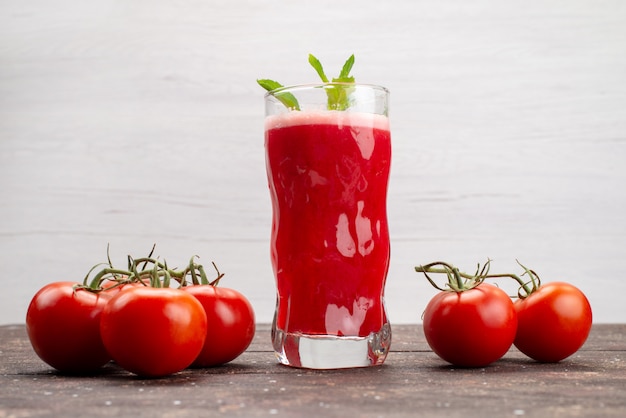 Vista frontal de jugo de tomate fresco con hojas junto con tomates enteros en cóctel de color gris, fruta vegetal