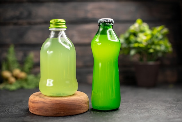 Vista frontal de jugo verde en botella en limonada de tablero de madera sobre superficie de madera oscura.