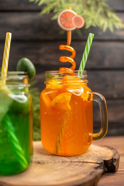 Vista frontal de jugos de frutas frescas en un vaso servido con tubos sobre una tabla de cortar de madera sobre una mesa marrón