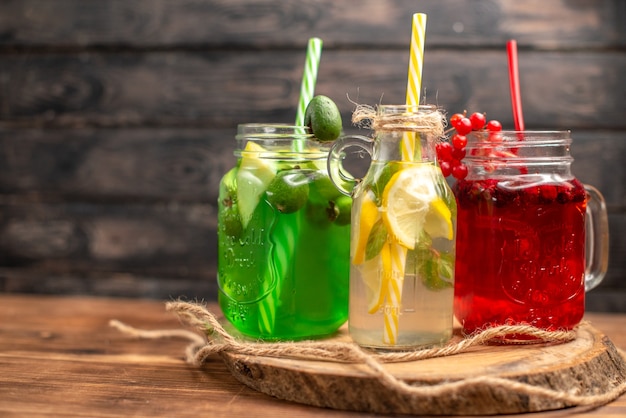 Vista frontal de jugos de fuit orgánicos naturales en botellas servidas con tubos sobre una tabla de cortar de madera