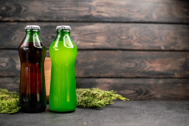 Vista frontal jugos negros y verdes en botellas ramas de pino en mesa de madera