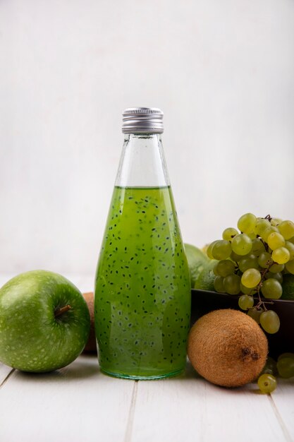 Vista frontal de kiwi con botella de jugo de manzana y uvas en la pared blanca