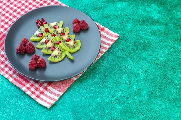 Vista frontal de kiwis frescos en rodajas con frambuesas en la superficie verde de bayas de frutas exóticas foto color tropical