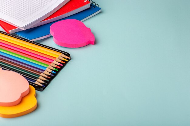 Vista frontal de lápices de colores con cuadernos sobre superficie azul