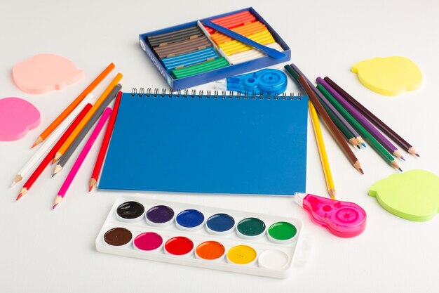 Vista frontal de lápices de colores con pinturas y pegatinas en el escritorio de color blanco claro
