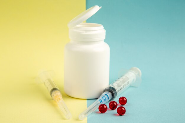 Vista frontal lata de plástico blanco con inyecciones y pastillas rojas sobre fondo amarillo-azul