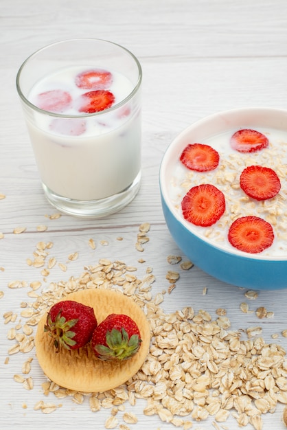 Vista frontal de leche con avena dentro de la placa con fresas junto con un vaso de leche en blanco, leche de desayuno de leche saludable