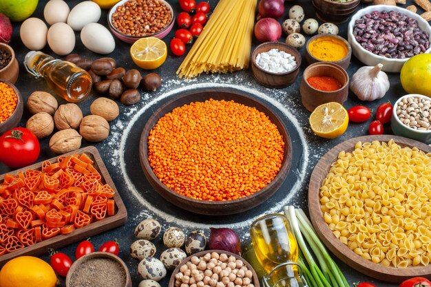 Vista frontal de lentejas naranjas con nueces, huevos, verduras, pasta cruda y condimentos sobre fondo gris oscuro, comida cruda, dieta, cocina, foto en color, nuez, frijol