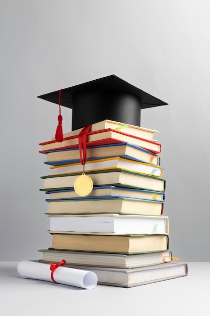 Vista frontal de libros apilados, una gorra de graduación y un diploma para el día de la educación