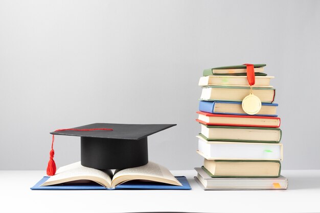 Vista frontal de libros apilados, una gorra de graduación y un libro abierto para el día de la educación