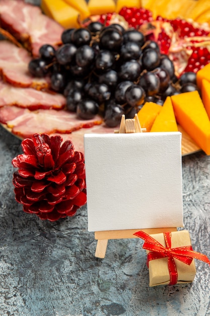Foto gratuita vista frontal lienzo blanco sobre caballete de madera uvas piezas de queso rebanadas de carne en placa de madera detalles de navidad en la oscuridad