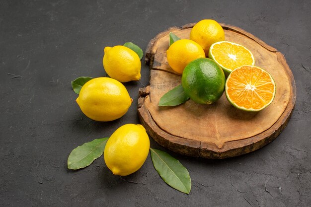Vista frontal de limones agrios frescos con hojas sobre fondo oscuro