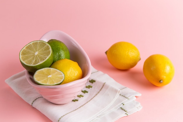 Vista frontal de limones frescos con rodajas de limón dentro de la placa en la pared rosa claro