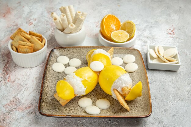 Vista frontal de limones helados con caramelos y galletas en la bebida de frutas cóctel de jugo de mesa blanca