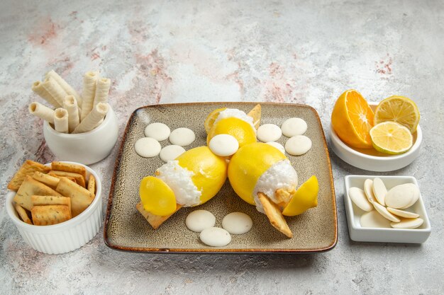 Vista frontal de limones helados con caramelos y galletas en la bebida de frutas de cóctel de jugo de mesa blanca