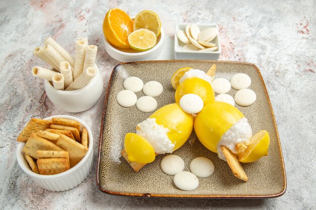 Vista frontal de limones helados con caramelos y galletas en el jugo de mesa blanca cóctel de frutas