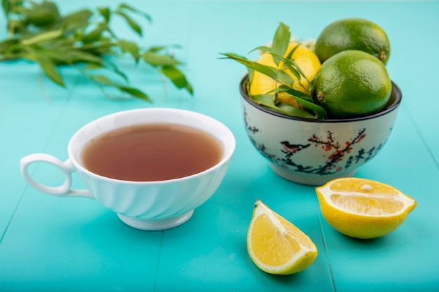 Vista frontal de limones en un recipiente con una taza de té en rodajas de limón sobre la superficie azul