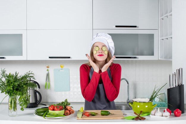 Vista frontal linda cocinera en uniforme poniendo rodajas de pepino en su cara